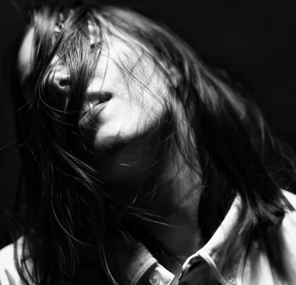 Hair blown across the face, only a piece of the cheek lit against the dark