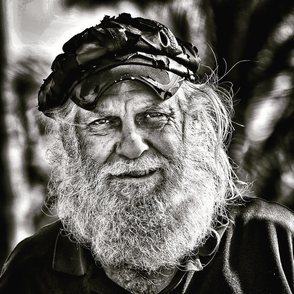 An older man with a thick beard in a cap, his face drawn out by its lines