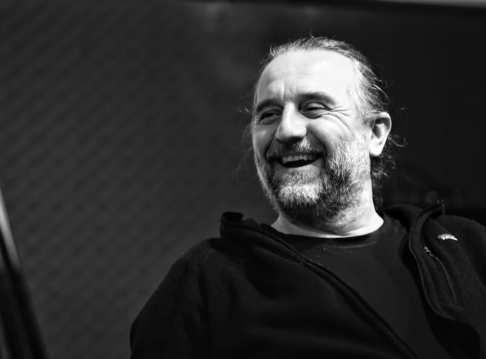 A bearded man in dark clothing laughing, the light coming from the side