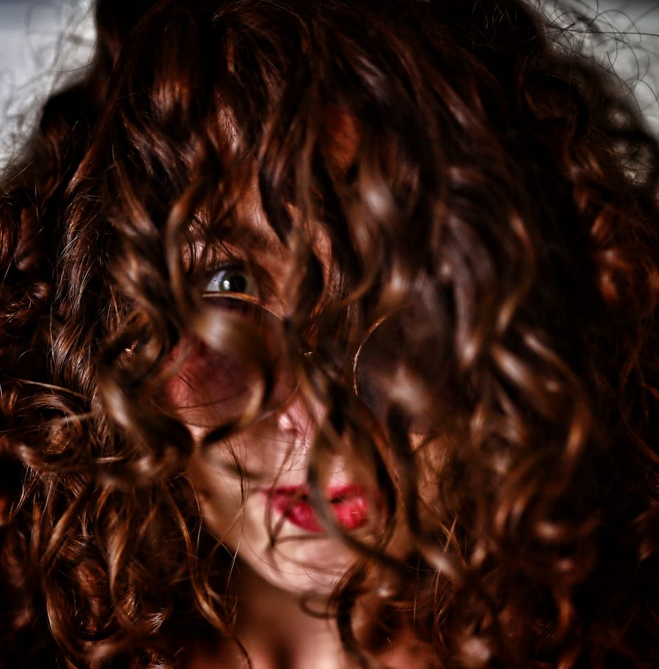 Red curls across the face, red lips and one eye showing between them
