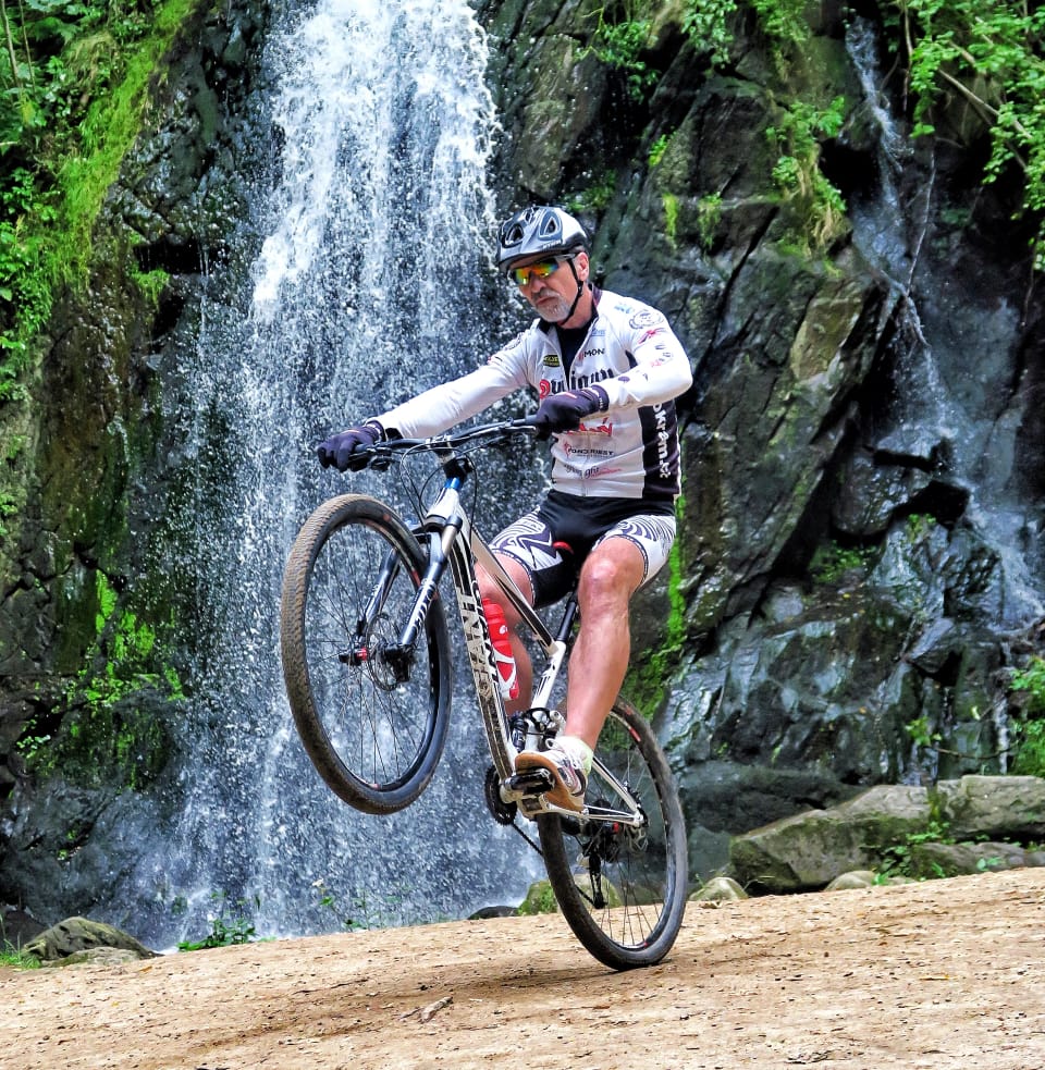A mountain biker riding a wheelie in front of a wall of falling water