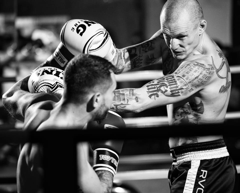 Close in on the boxing ring: a punch lands on the opponent's head, both bodies drawn into a single instant