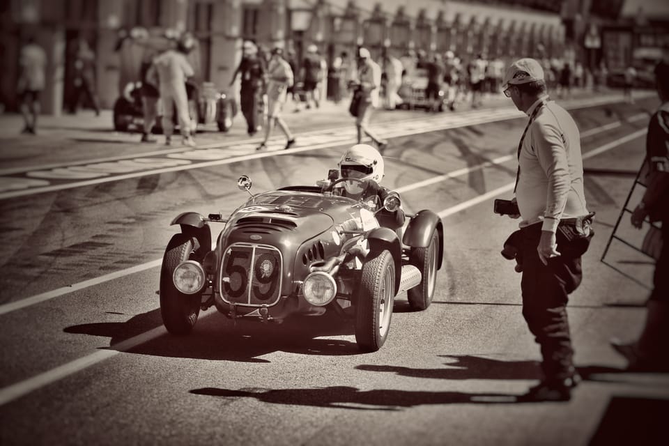 The pit lane in a toned rendering, a historic car among people like a scene from another era