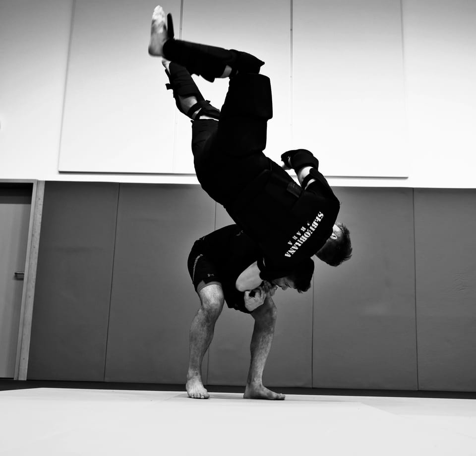A dancer in a headstand against a bare wall, the body squared into a vertical