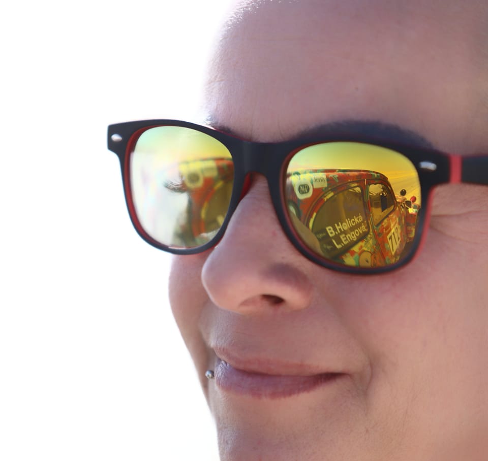A face in mirrored sunglasses, a race car reflected in the lens