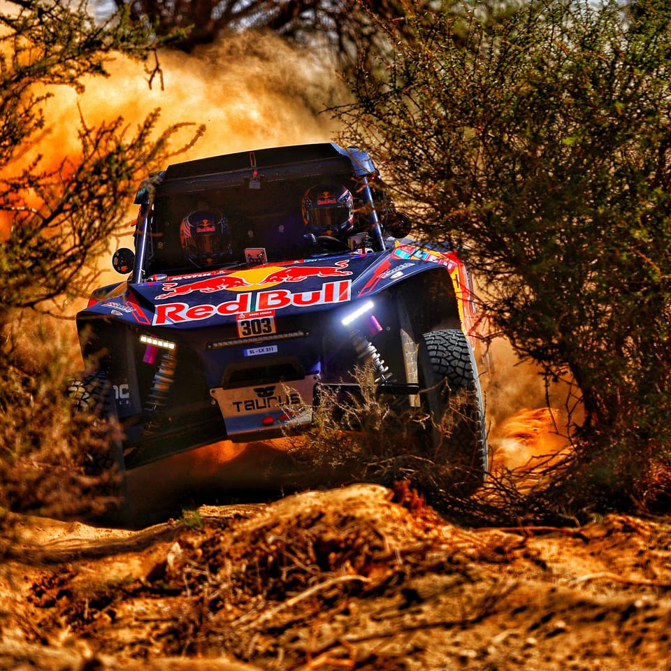 A buggy bursting through desert scrub, dust and branches flying aside