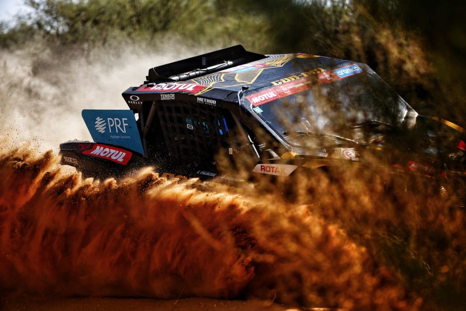 A racing buggy at full speed, throwing a cloud of rust-coloured dust from its wheels