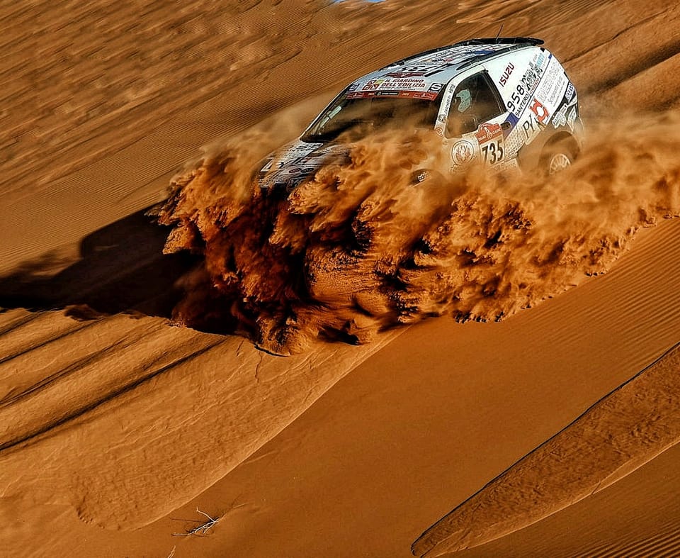 A Dakar car descending a dune, trailing a long plume of sand