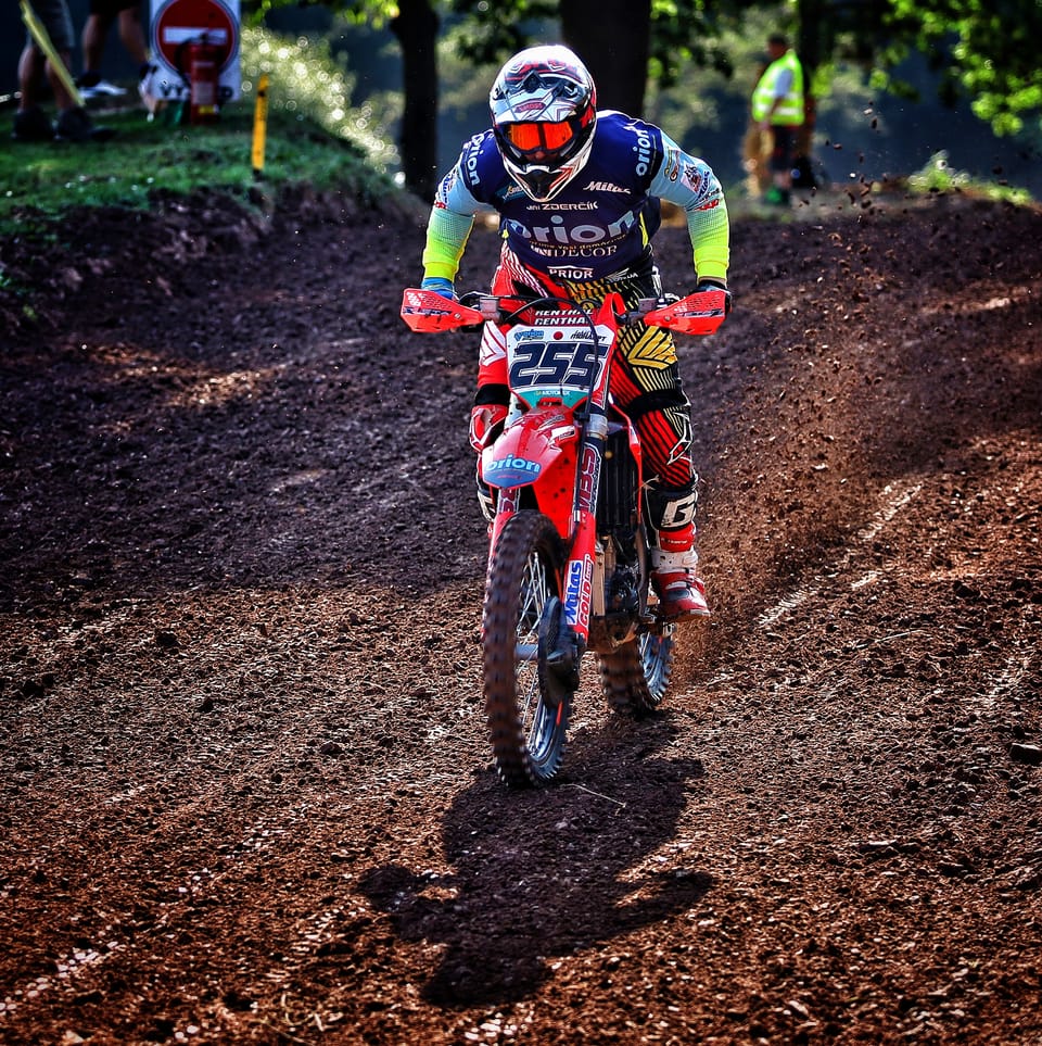 Rider number 255 on a broken forest track, trees and spectators around