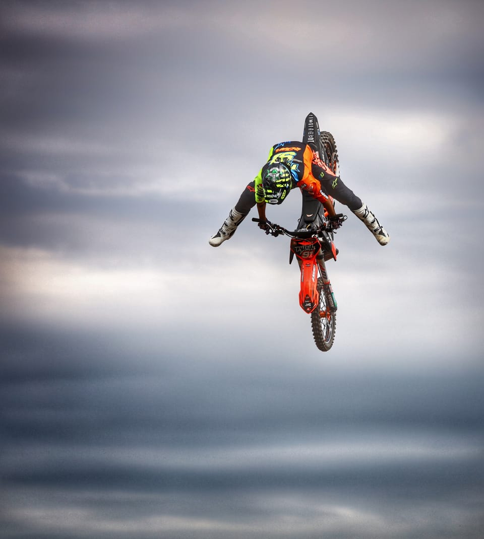 A freestyle rider upside down beside his bike against a grey sky