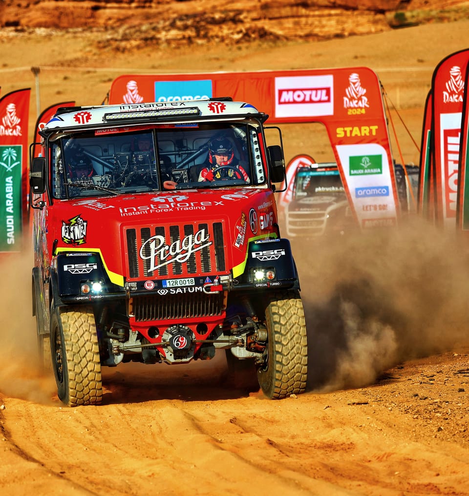 A red racing truck pulling off the start ramp into the dust