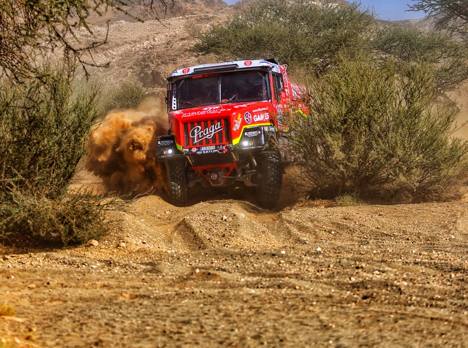 A red racing truck at full speed between the scrub, wheels off the ground