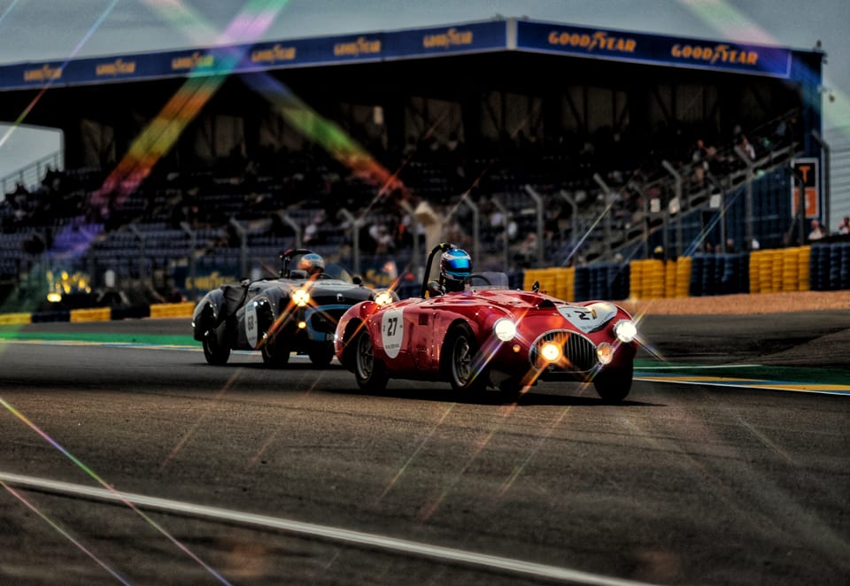 Historic race cars through a circuit corner, grandstand behind