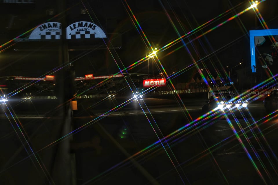 The circuit at night, lights drawn into rays, the Le Mans sign above the track
