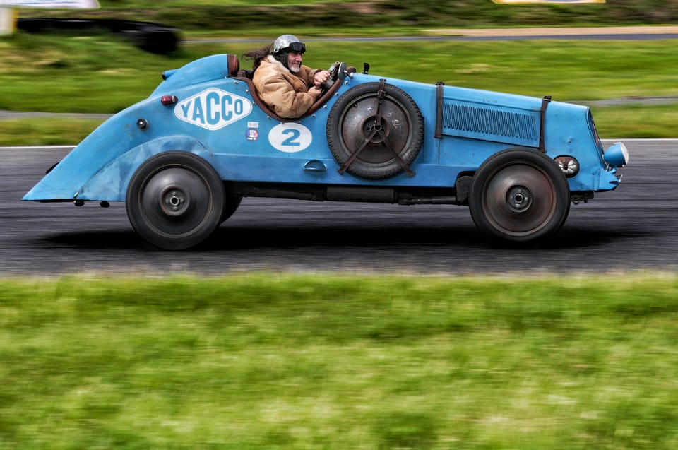 A pale blue single-seater passing side-on, its wheels blurred by rotation