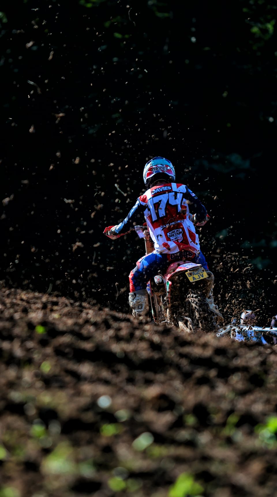 Rider number 74 from behind, clods of earth flying from the wheel into darkness
