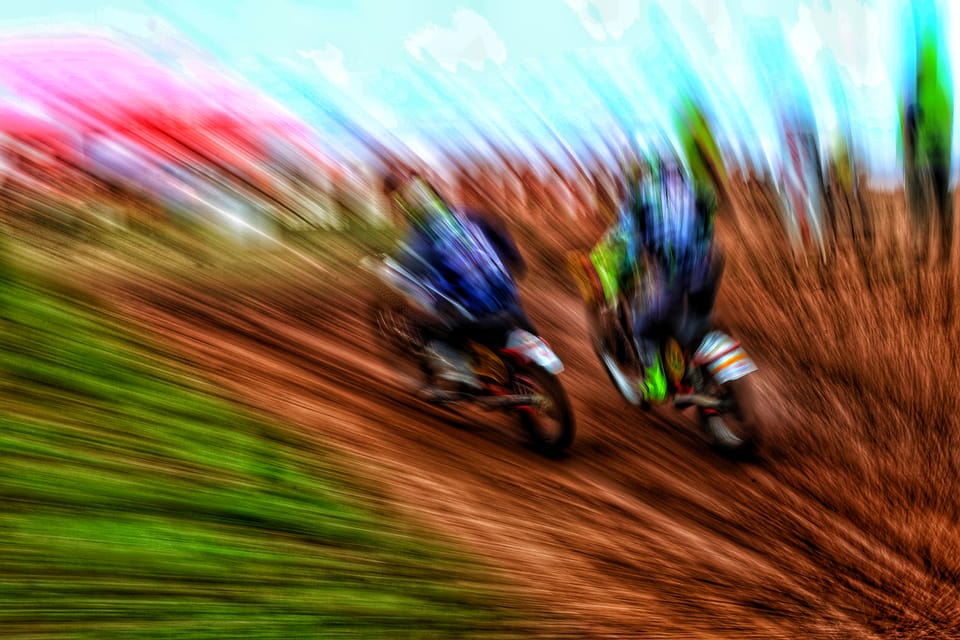 Two motocross riders battling, captured with a zoom blur that pulls the scene into streaks of colour