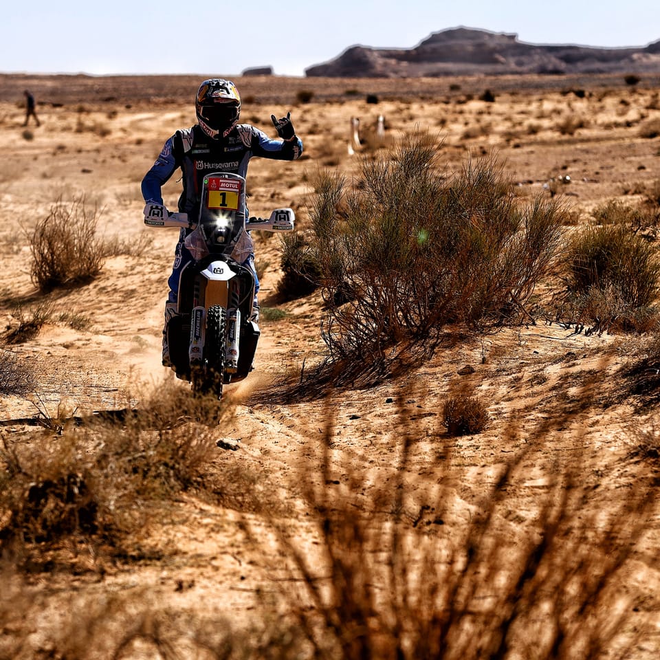 A motorcyclist on a desert track between low scrub, nothing around but stone and sand