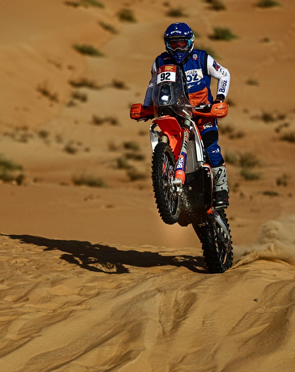 A motorcyclist standing on the pegs crossing the crest of a dune