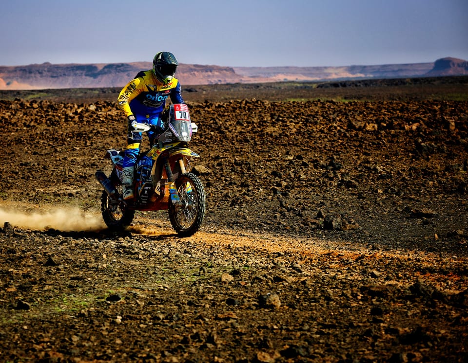 A Dakar rally motorcyclist crossing stony desert, mesas on the horizon