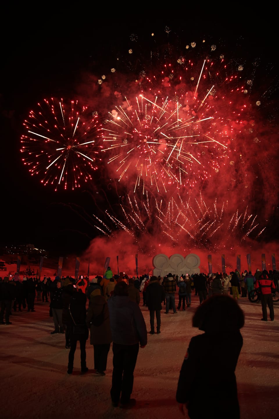 Red fireworks above a crowd, figures silhouetted against the glare