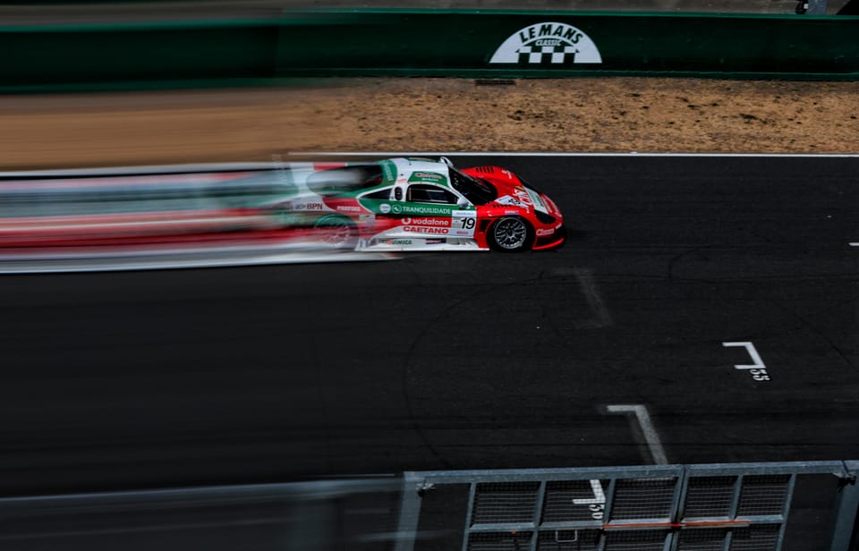 A red car on the circuit, barriers and tarmac drawn into horizontal streaks by the pan