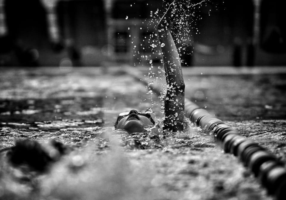 A swimmer's arm tearing the surface, droplets flung from the hand hanging in the dark above the lane