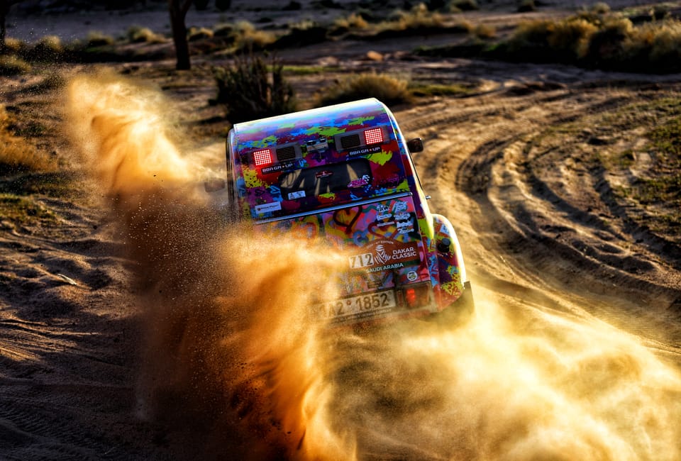 A brightly painted car burying itself in a cloud of flung sand