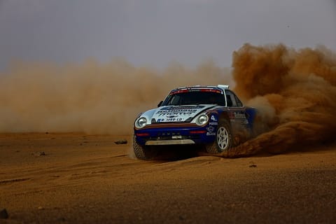 A rally Porsche on gravel, thick dust rising behind the car