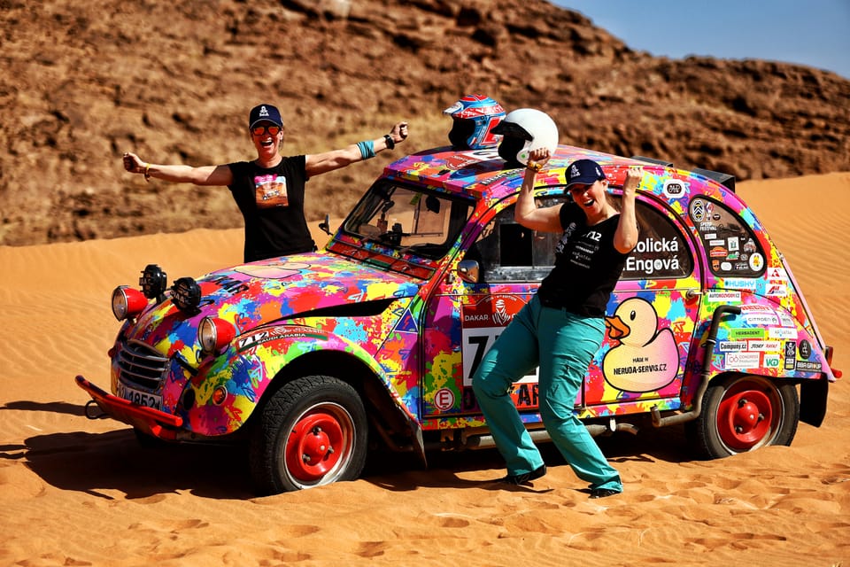 A crew posing beside their brightly painted car in the middle of the desert