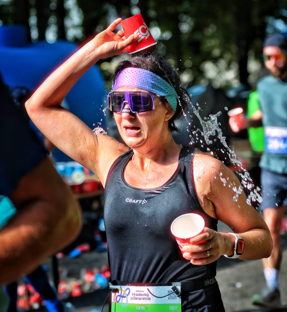 Běžkyně na půlmaratonu si na občerstvovačce lije kelímek vody na hlavu