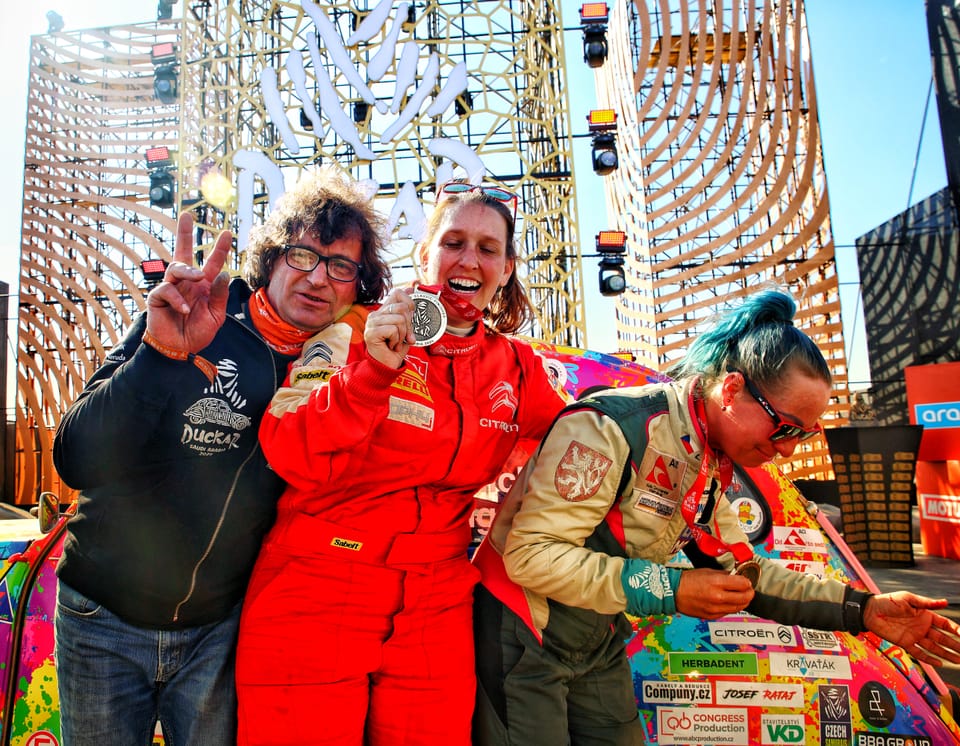Joy at the finish: a driver in red overalls with a medal between two other people