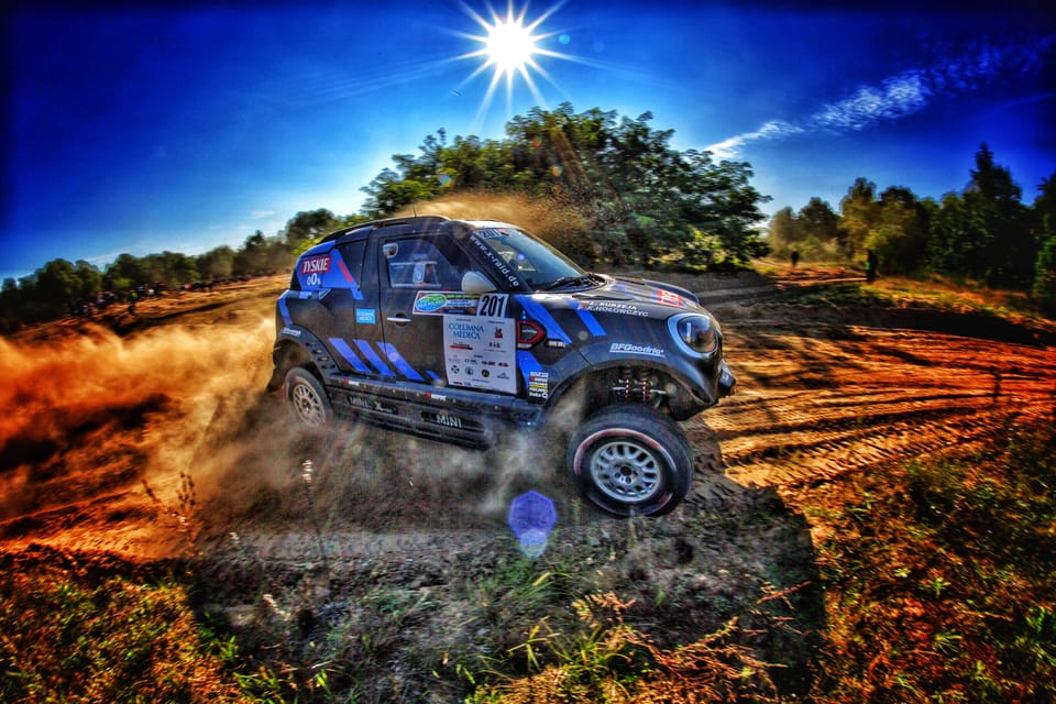 A rally car off-road, the sun directly above it split into a hard star
