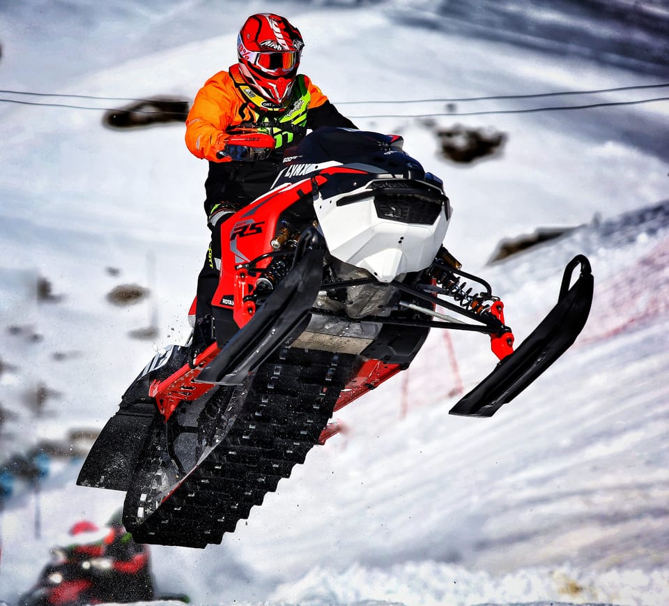 A snowmobile in flight above a frozen course, the rider in orange