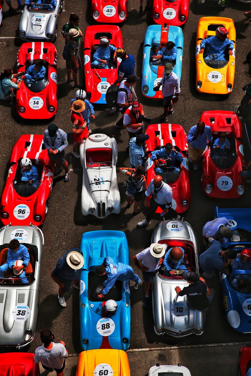 Looking down on a starting grid packed with colourful historic cars and people among them