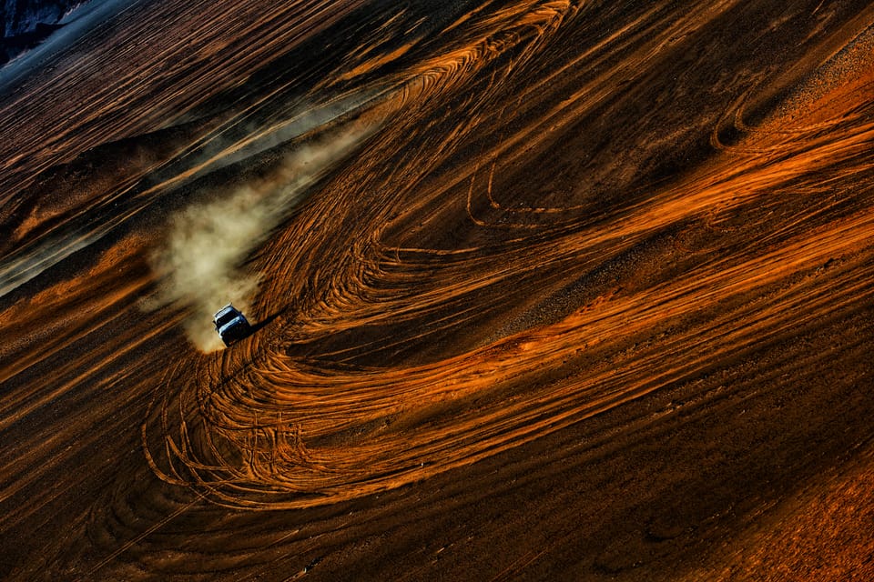 A vehicle drawing long arcs across the dunes, the whole frame held by sand and tracks alone
