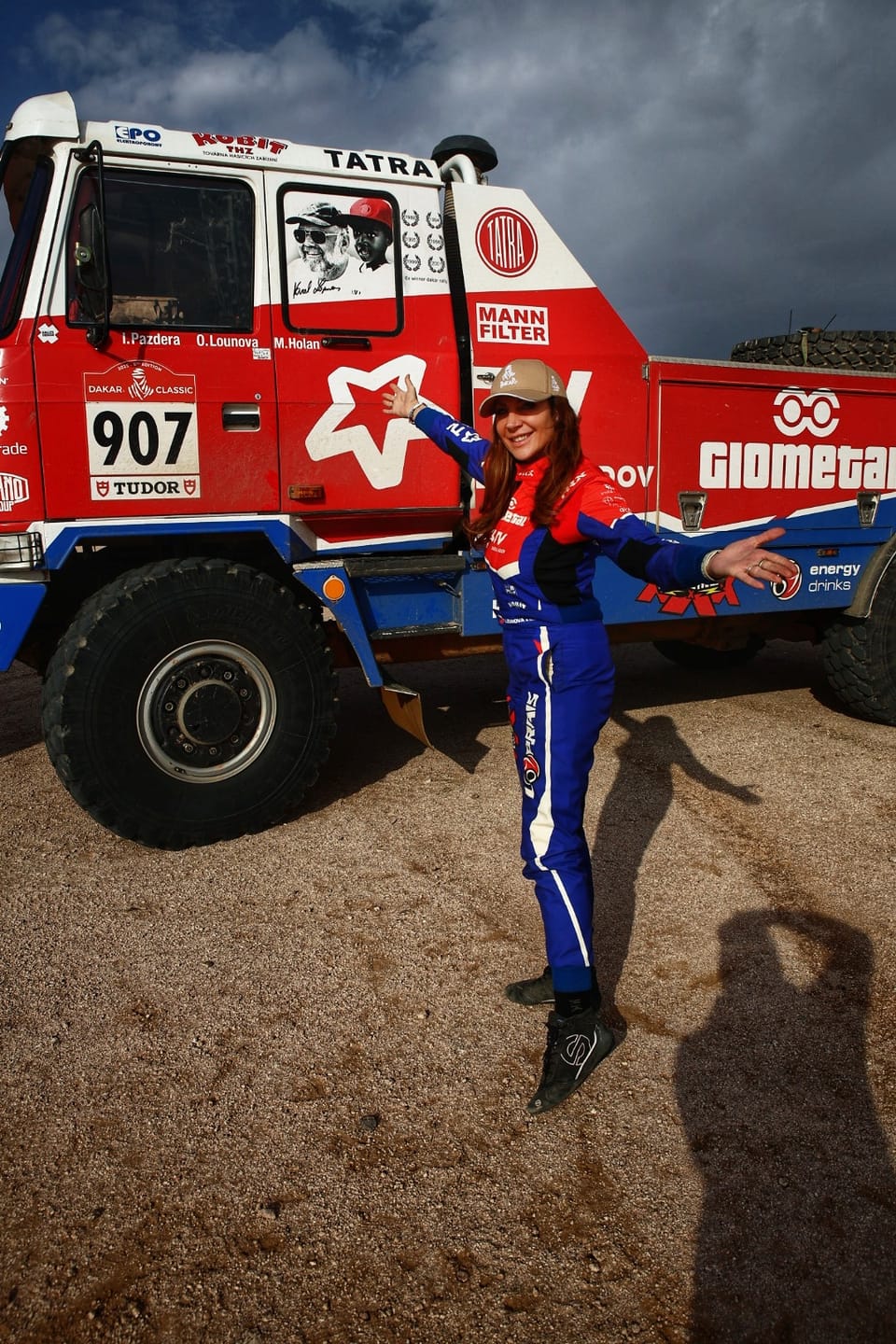 A driver in racing overalls in front of a competition Tatra truck, number 907