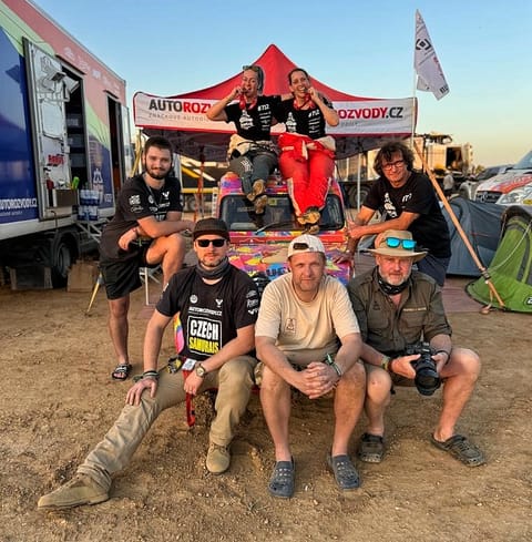 A team group shot at the bivouac, the crew seated on and around their painted car