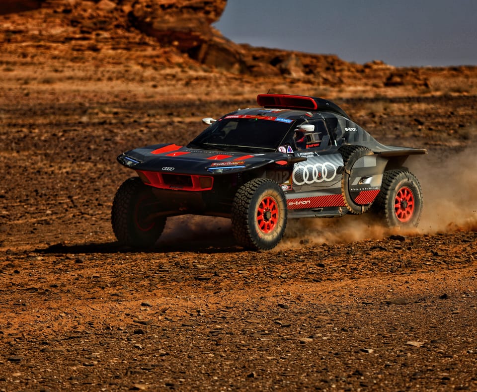 A low rally raid car on the red flats, dust rising behind it