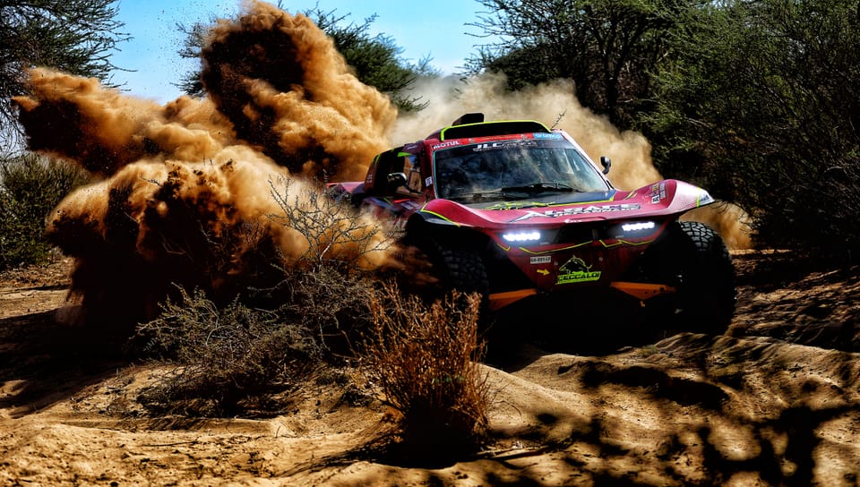 A race car tearing through desert scrub, dust blasting out to both sides